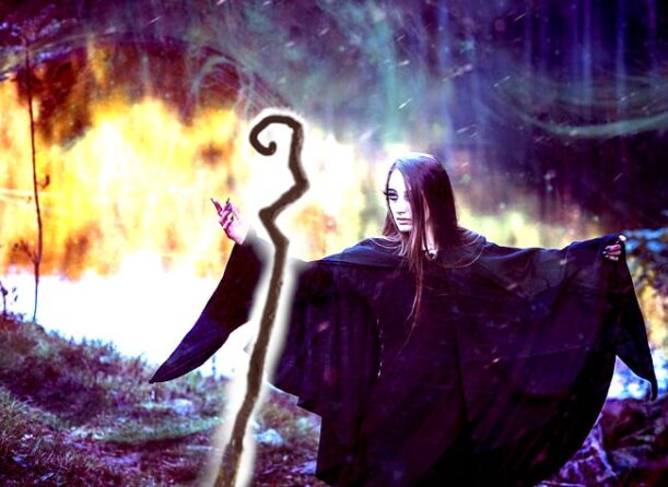 giovane strega vestita di nero che fa una magia, un incantesimo nel bosco con il bastone e il fuoco